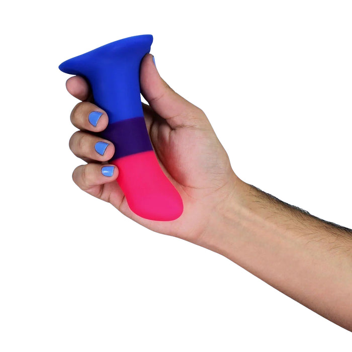 Hand holding a silicone dildo with pink top and blue bottom on a white background